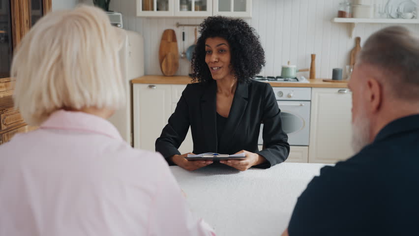 Real estate manager meeting with elderly couple in new house, discuss contract. Positive african american woman talking papers to clients and smiling, life and property insurance, agreement for credit