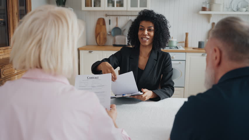 Real estate manager meeting with elderly couple in new house, discuss contract. Positive african american woman talking papers to clients and smiling, life and property insurance, agreement for credit