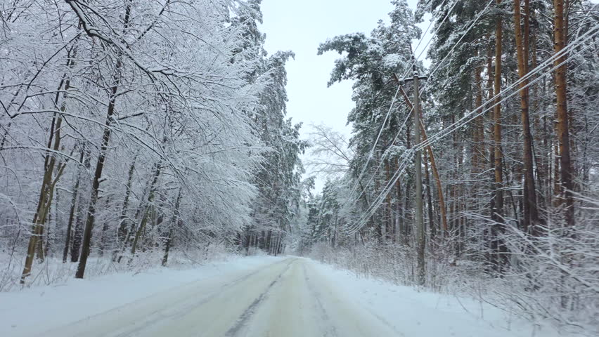 Car driving along snowy forest road in winter landscape, Winter journey through snow-covered forest road with icy conditions