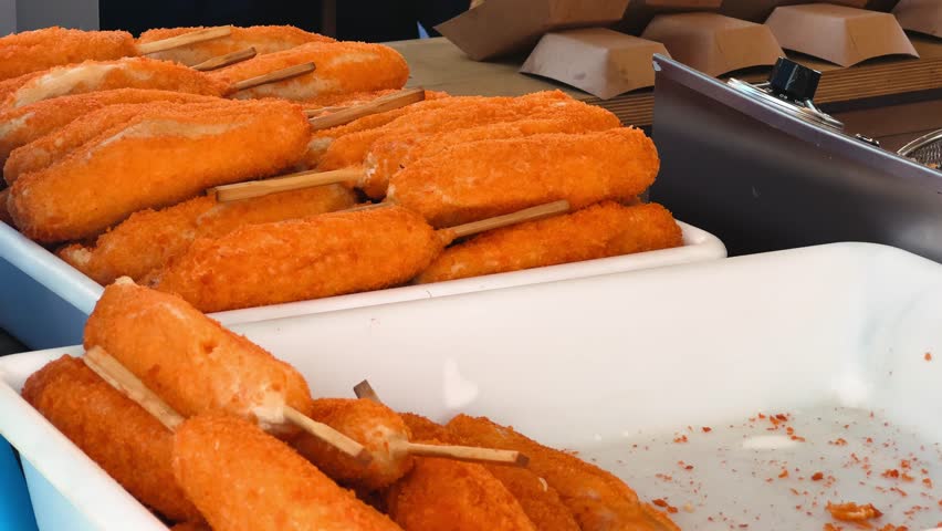 A crispy Corn Dog is freshly prepared at the street market. A juicy sausage on a stick is coated in thick batter and deep-fried to golden perfection. High quality 4k footage