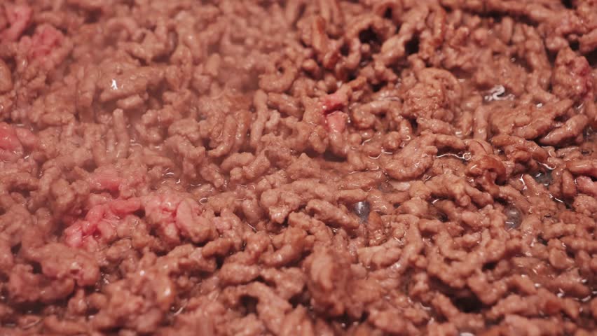 A close-up of fresh ground beef. The cook begins preparing pasta Bolognese and fries the ground beef in a pan. High quality 4k footage