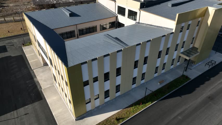 Aerial shot of a contemporary school facility featuring a red and green outdoor sports court, asphalt paths, and surrounding countryside landscape during daytime.