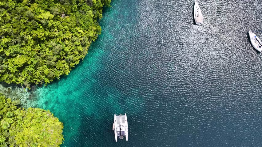 High angle drone shot captures yachts anchored in turquoise water beside lush limestone islands