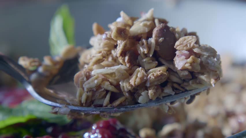 Close up motion of spoon scooping healthy granola cereal with berries and greens from bowl