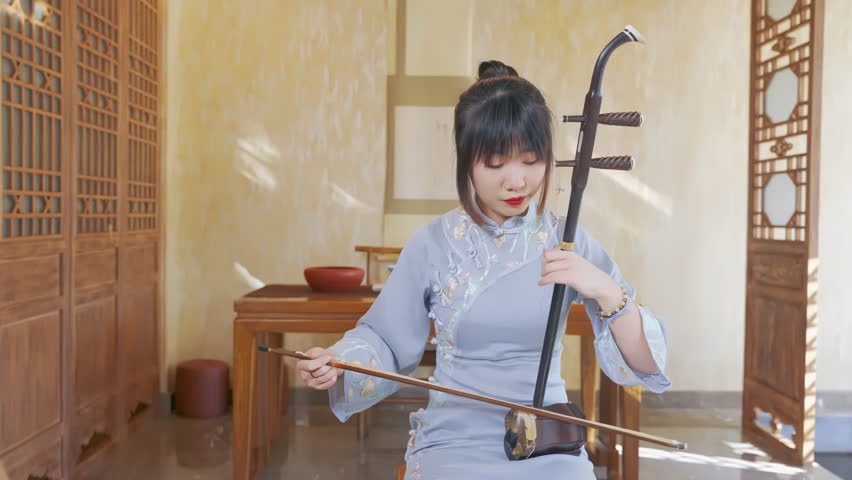 Beautiful young expertly musician playing Chinese two-stringed bowed musical instrument, focused on strings, bow movement, and musical expression. The bow moves smoothly across the strings