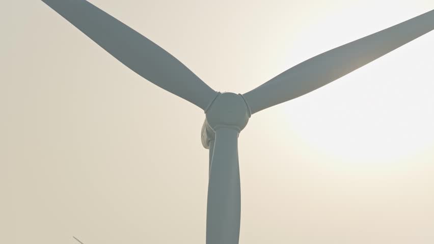 Single wind turbine close up with rotating blades at sunrise. A windfarm in the background is generating renewable energy on a foggy morning