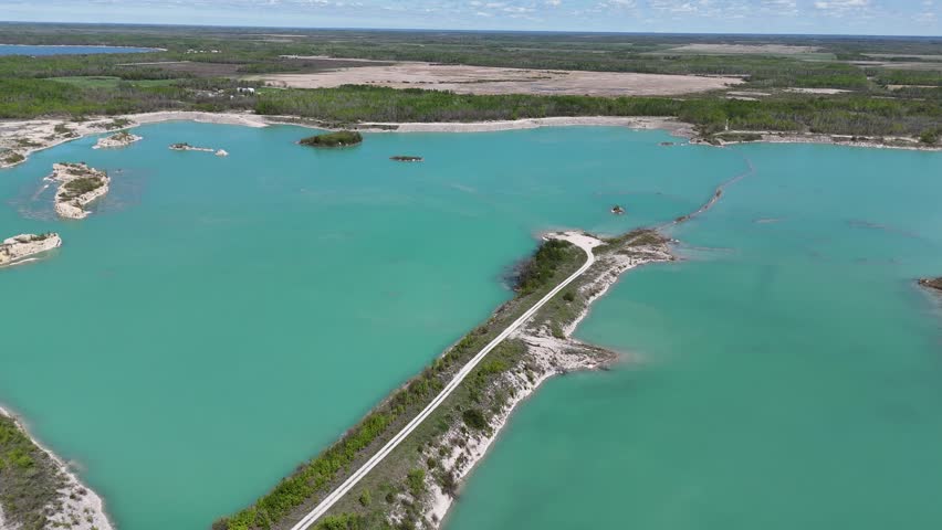 Drone flying forward over Steep Rock Manitoba limestone quarry, panning right to reveal a long spit of land with a hiking trail, quarry cliffs, islands, and boreal forest under cloudy summer skies.