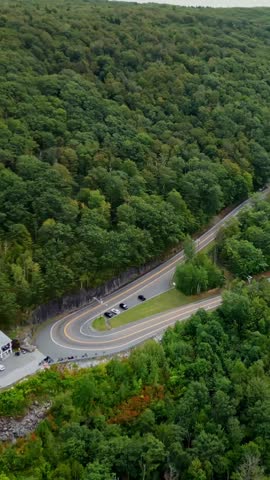 Cars driving along a sharp hairpin curve on the scenic Mohawk Trail in the Berkshire Mountains of Massachusetts surrounded by dense green forest.