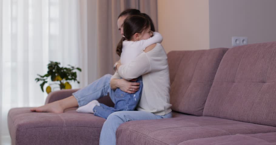 Young mom and her little daughter playing, laughing, and tickling each other on the couch at home