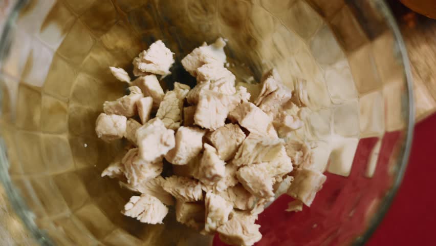 Top view of transferring boiled chicken chunks into a glass bowl