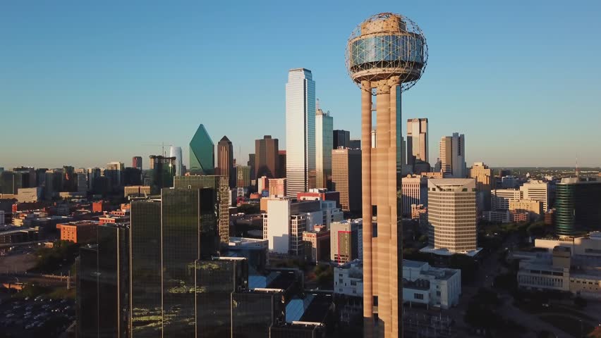 Aerial drone footage captures Reunion Tower and Dallas skyline at sunrise with blue sky