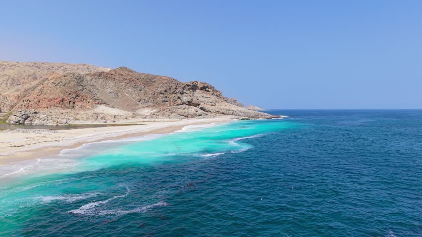 Aerial view of turquoise ocean water meeting a white sand beach and rugged desert mountains along the Red Sea coast, Saudi Arabia.