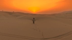 Aerial view of a young woman walking across sand dunes toward the setting sun in the desert of Oman. - Powered by Shutterstock - Get 15% off with code: PIKWIZARD15