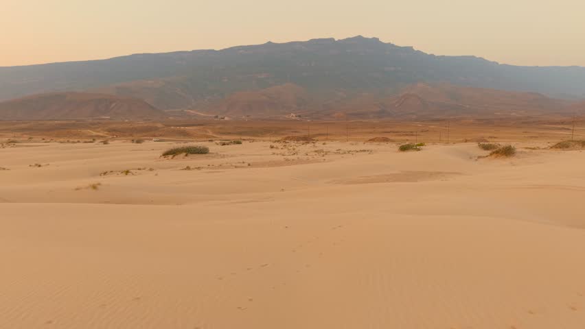 Aerial view of sand dunes and desert plains extending toward distant mountain ranges in Oman.