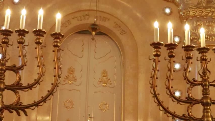 Horizontal cinematic tilt up from dark wooden entrance doors to bright arched Star of David stained glass window in historic synagogue