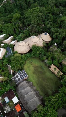 Vertical aerial footage of Green School Bali featuring sustainable bamboo architecture surrounded by dense tropical forest and lush green landscape in Indonesia.