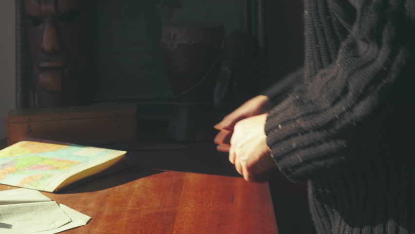 Medium shot of a person unfolding a large, colorful vintage travel map of the United States on a warm, sunlit table. Evokes trip planning vibes.