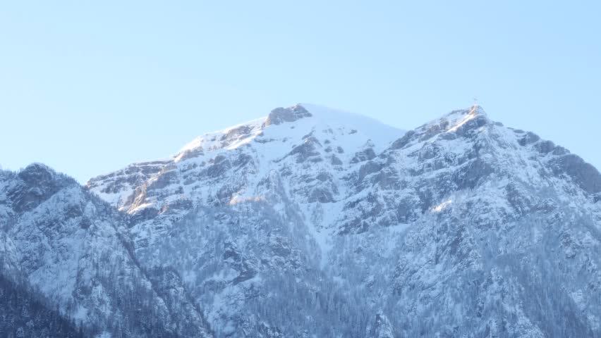 Close view of the snow-covered peaks of the Bucegi Mountains in winter, rising above the town of Busteni in Romania. Scenic Carpathian mountain landscape under clear blue sky.