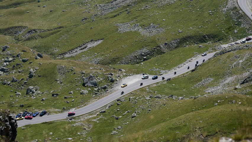 Wide pan right and upward along Transalpina road with cars driving through mountains