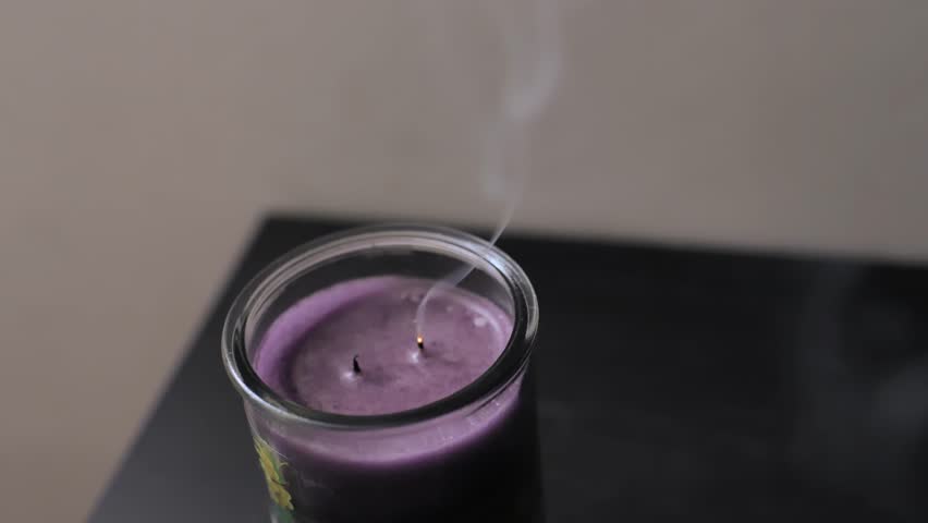Smoke plumes gently rise from the extinguished wicks of a purple candle, creating a serene and lingering visual