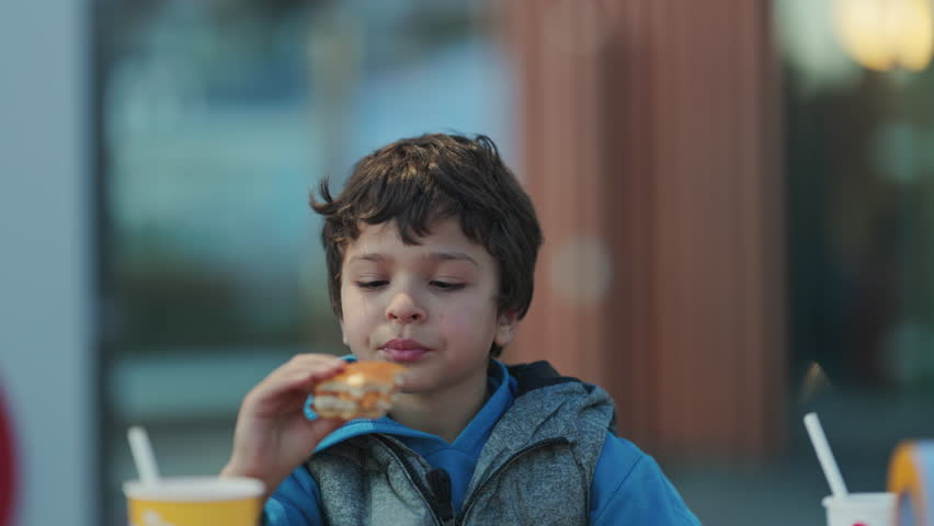Cute little boy happily eating burger at a fast food restaurant