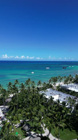 Aerial vertical shot of the turquoise Caribbean Sea, sandy beaches, and luxury resorts at Punta Cana coastline with boats in the water