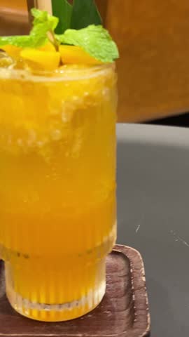 Pouring mango smoothie in a glass with fresh mango, mint and lime.