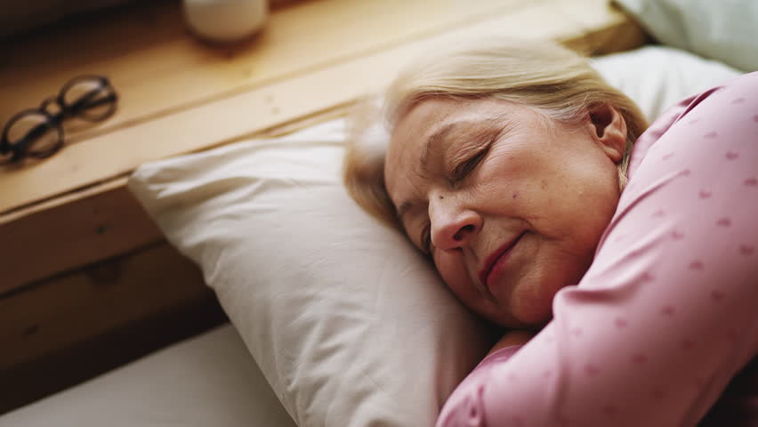 Blond senior woman lying on orthopedic pillow, enjoying healthy morning sleep