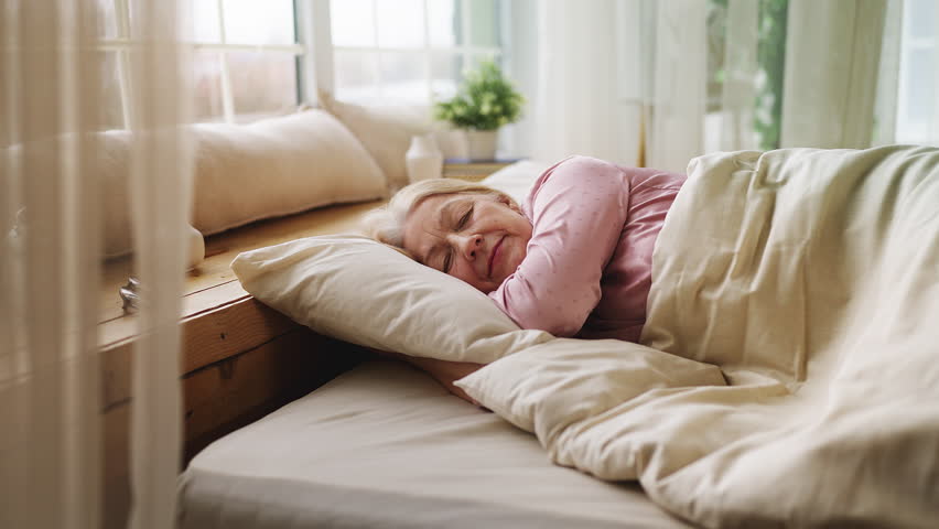 Peaceful senior woman sleeping in morning light in bed, healthy rest and comfort