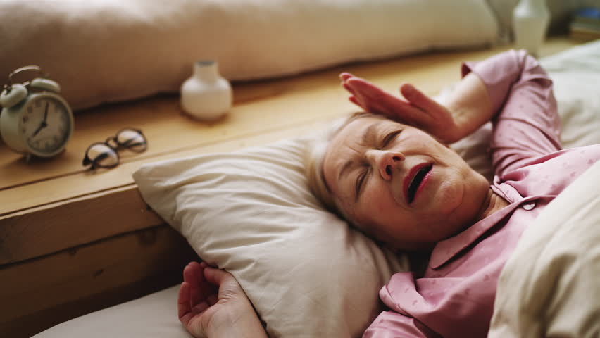 Happy senior female waking up in cozy bed and stretching, morning energy