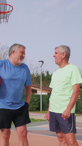 vertical Two active senior men having fun and sharing a laugh while playing basketball on an outdoor court, demonstrating a healthy and sporty lifestyle in their golden years through friendship and exercise