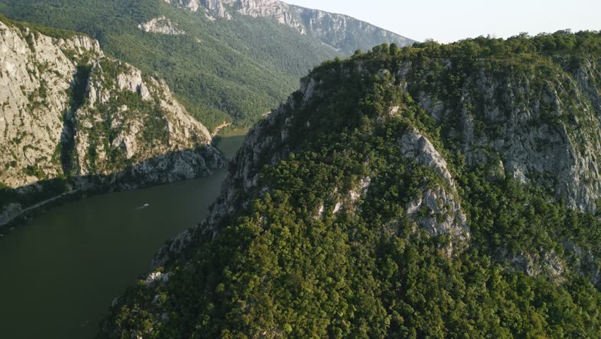 Aerial drone shot flying backward and panning left over Danube river canyon at Iron Gates, dramatic cliffs and forested mountains in Romania scenic landscape