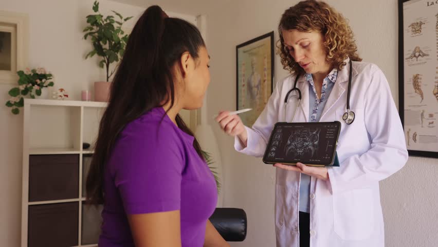 Professional female doctor showing a patient her hip x ray results on a digital tablet, explaining the diagnosis in a clinic