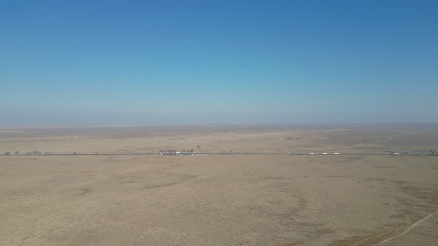 Wide aerial perspective of a long road through vast, arid plains.