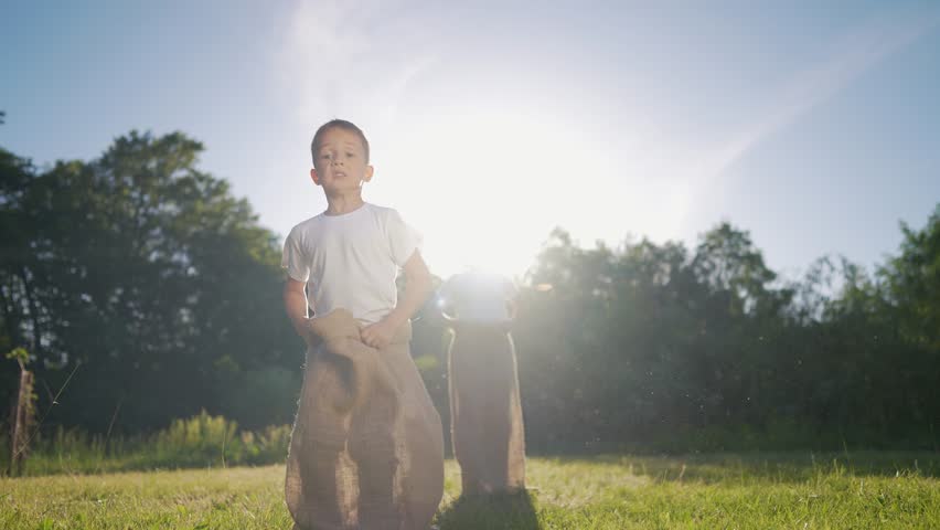 Two boys in field. Children race in sack outdoors. A young girl is playing with a teddy bear in the grass and is very competitive and energetic. A pair of boys lifestyle in a meadow.