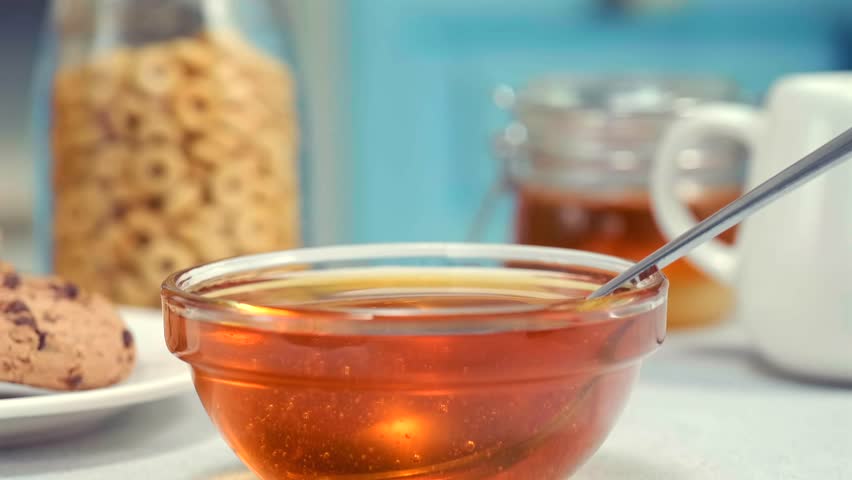 Honey dripping from spoon into glass bowl macro food texture dessert syrup copy space