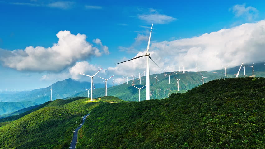 Aerial view of wind turbines on green hills under a clear blue sky. Renewable energy concept