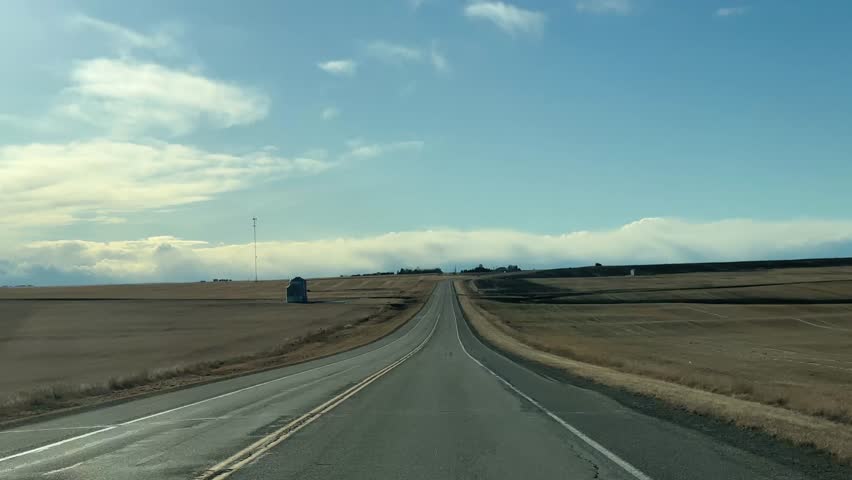 Forward-facing POV driving footage along an open highway on a clear sunny day in rural Alberta, Canada. The road stretches toward the horizon with bright blue skies and natural daylight illuminating the surrounding prairie landscape. Ideal for themes of travel, transportation, freedom, road trips, and scenic countryside driving.