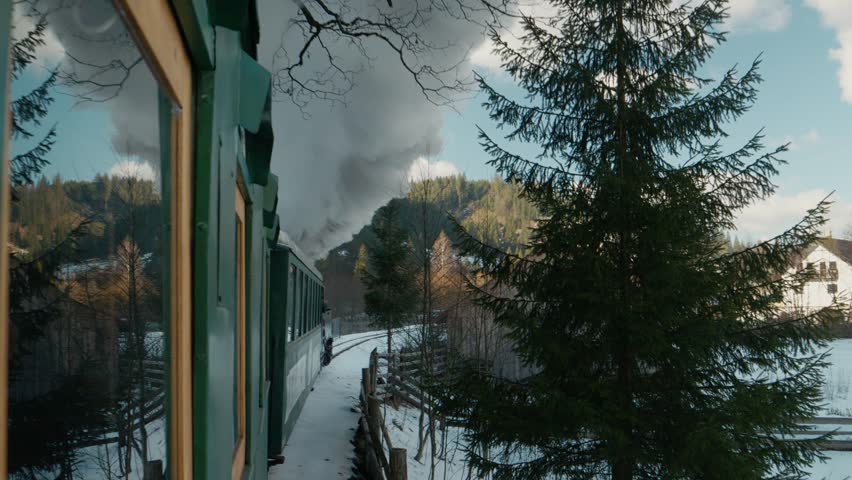 Mocanita steam train moves through the villages of Bucovina, Romania. The train releases thick smoke as it journeys along scenic tracks surrounded by nature.