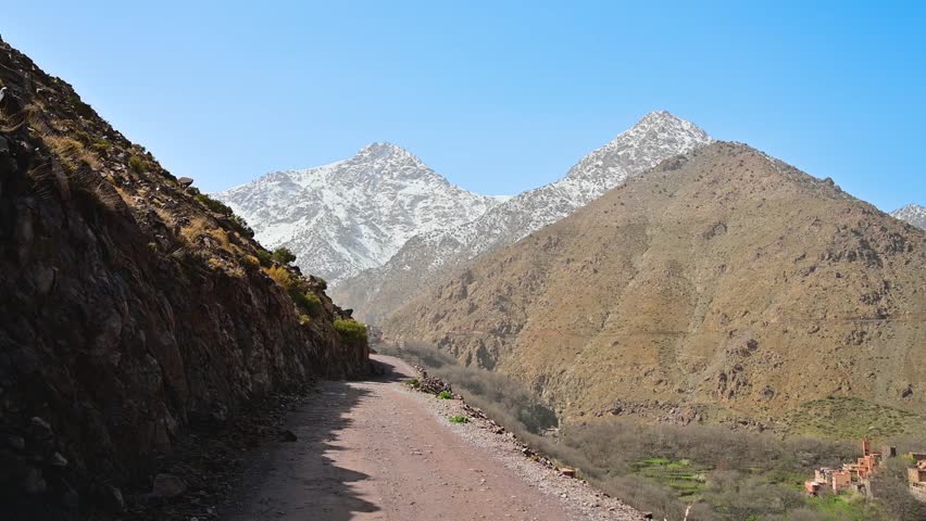 Beautiful point of view perspective walking a dusty trail towards the snow capped Mount Toubkal on a sunny day in the Atlas Mountains in Morocco