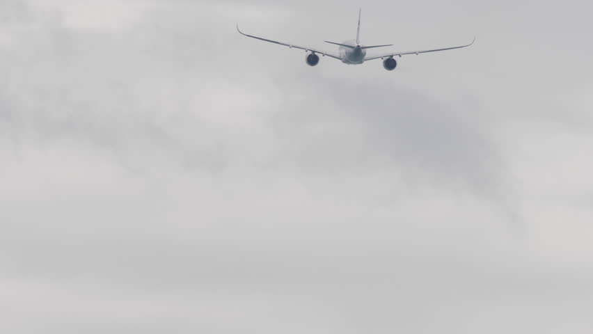 Back view of a commercial airliner climbing into the cloudy sky after takeoff. Symbolic image of aviation, travel, and freedom