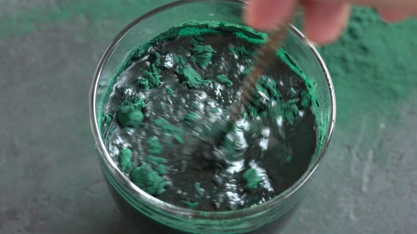 Stirring spirulina algae powder in a glass of water with a spoon. Nutritional supplement.