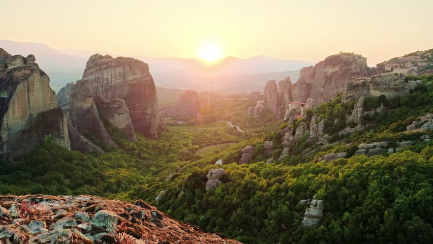 Majestic sunset landscape over the Meteora monastery complex, Greece. Ancient stone pillars and orthodox monasteries under a golden sky. Steadicam revealing footage