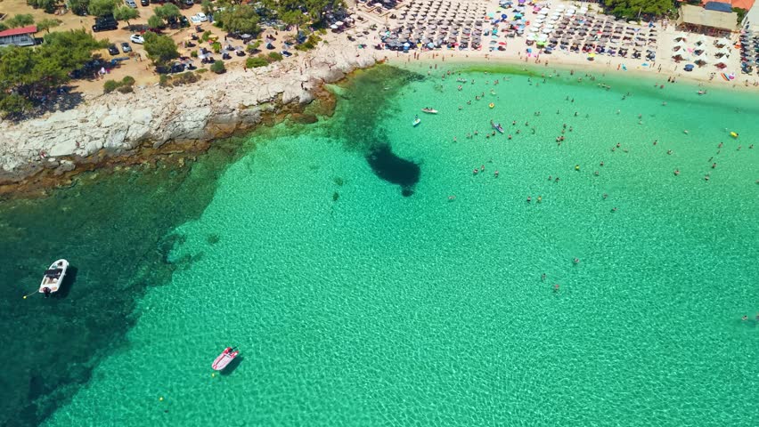 Aerial view of many people swimming in emerald water and sunbathing under umbrellas at Psili Ammos beach, Thassos island, Greece 
