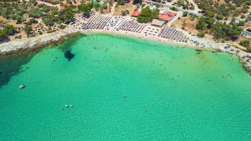 Aerial view of many people swimming in emerald water and sunbathing under umbrellas at Psili Ammos beach, Thassos island, Greece 