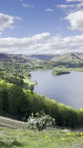 Panoramic view of Grasmere Lake, surrounding hills and Rydal Water under a blue sky with scattered clouds, seen from a high hillside. Lake District, England, UK.