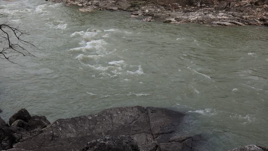 Fast mountain river flowing over rocks creating white water rapids natural landscape scene with strong current turbulent stream and rugged riverbank environment