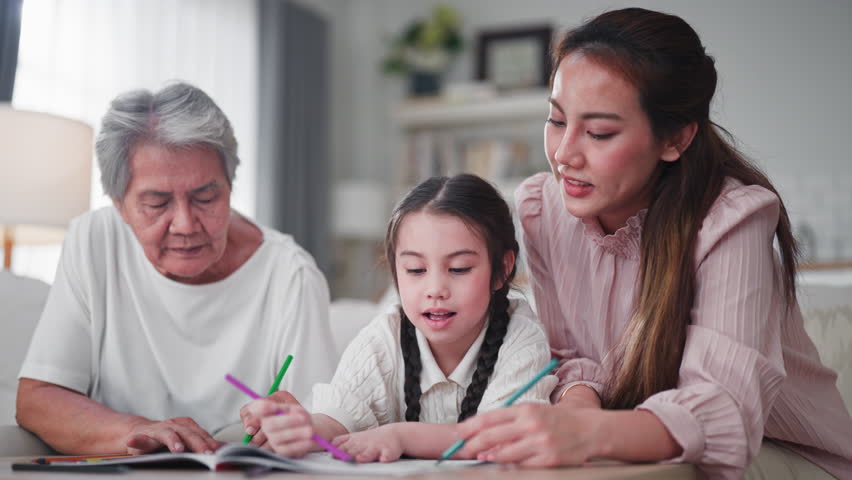 Grandmother and mother sit closely with a young girl, guiding her as she colors in a book with bright pencils, sharing a warm three-generation learning moment at home.