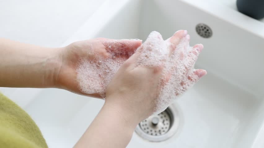 Woman washing hands with soap above white sink, closeup. Camera moving forward
