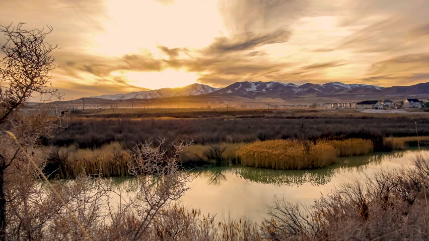Fiery sunset over a tranquil river flowing through a natural wetland with mountains in the background